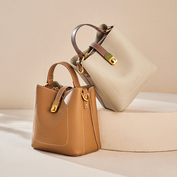 Two elegant women's bucket bags, one in tan and one in off-white, with gold hardware.