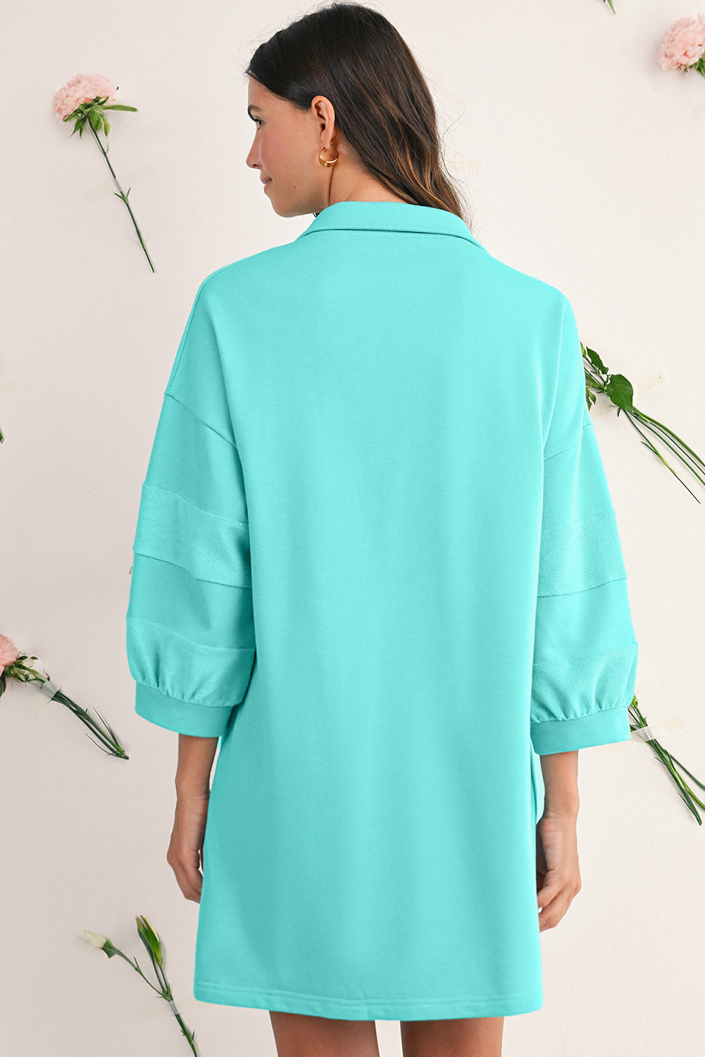 Person wearing a turquoise dress with floral decorations in the background