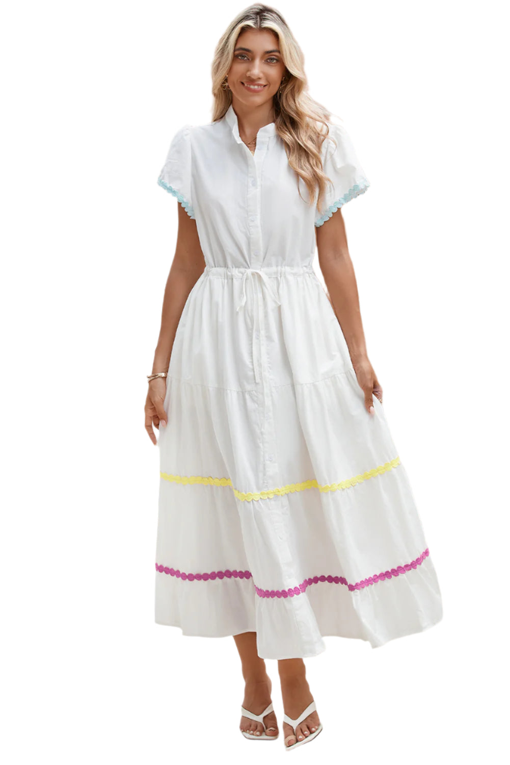 Model standing and smiling in a white tiered shirt dress with short sleeves and a waist tie, showcasing a stylish and cheerful look.