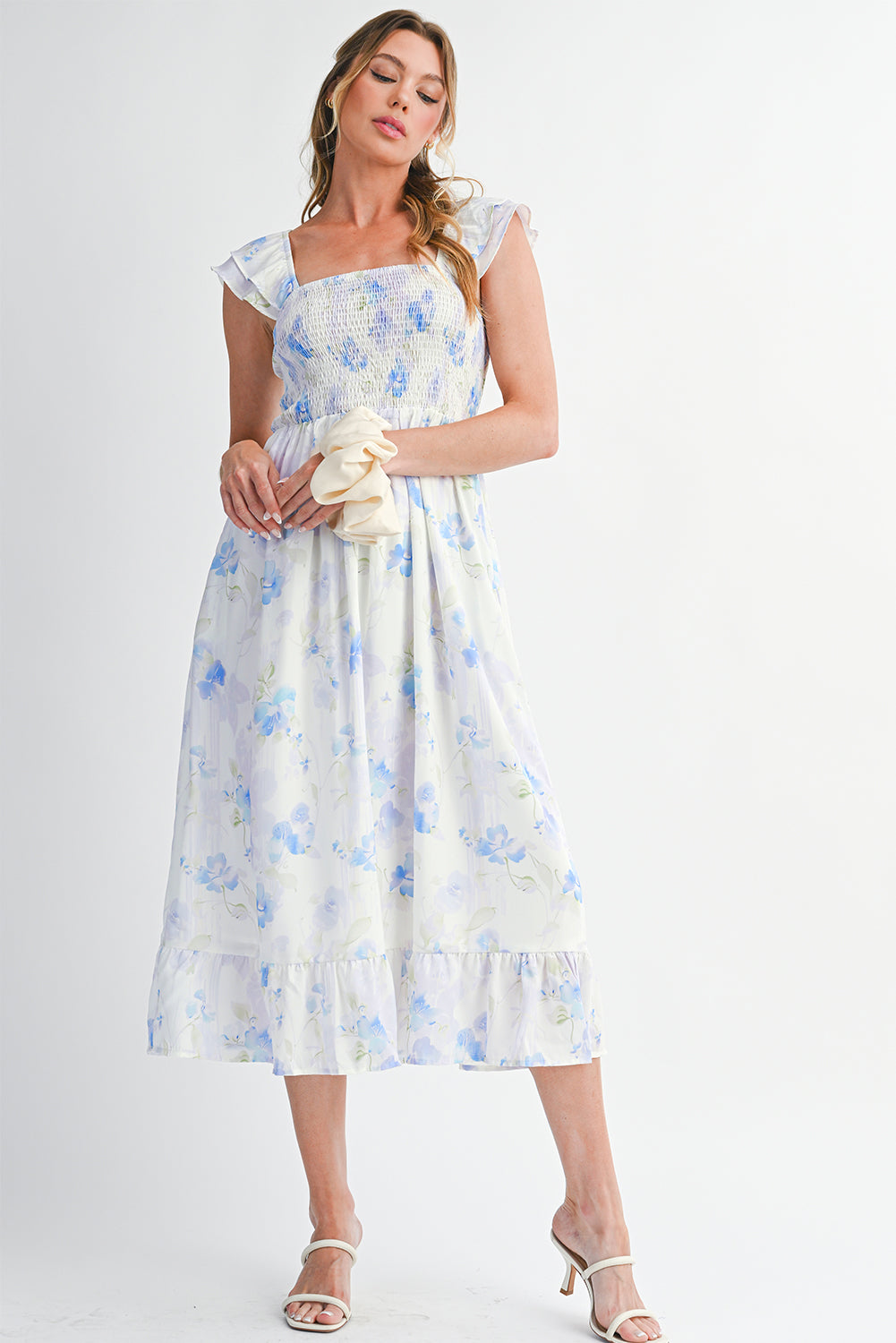 Woman wearing a floral dress holding a clutch against a white background
