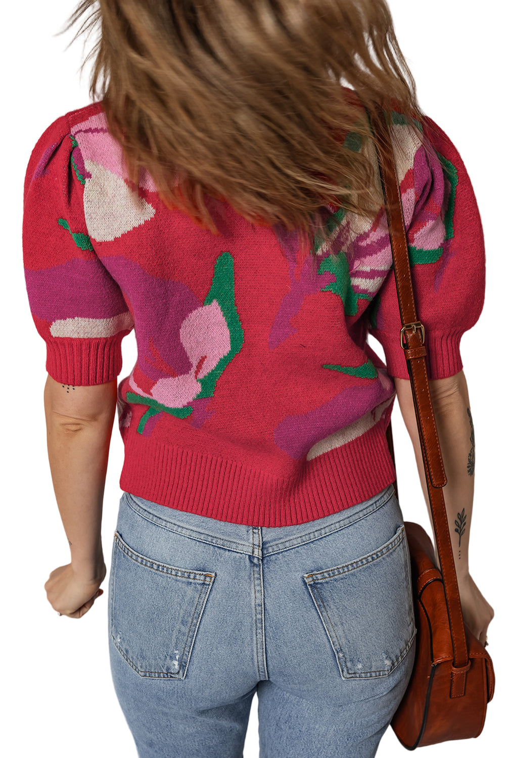 Person wearing a red floral sweater and blue jeans, holding a brown leather bag.