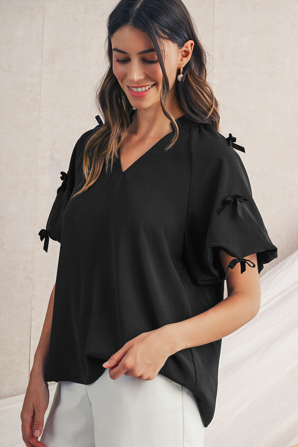 Woman wearing a black blouse with bow details on sleeves against a neutral background