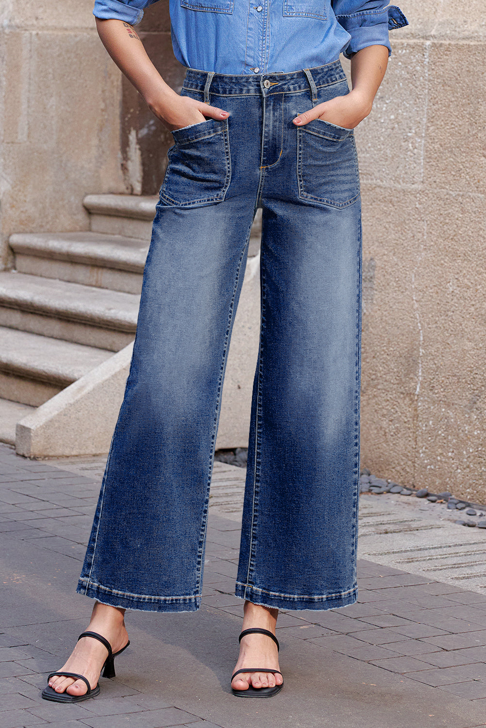Person wearing blue denim jeans and a matching shirt standing on a stone pavement.