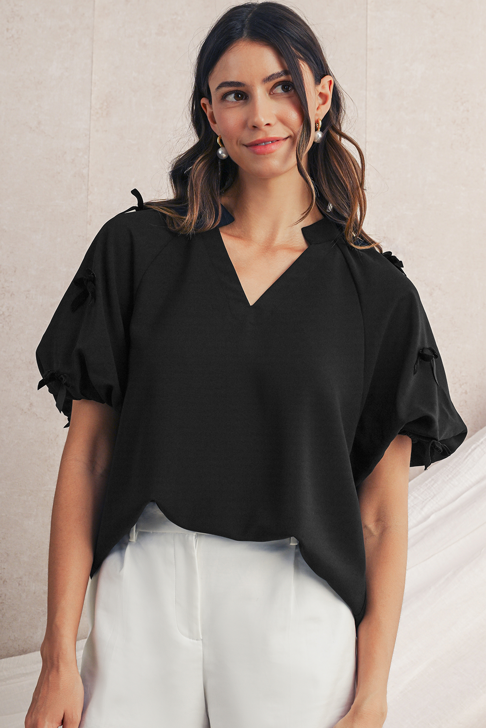 Woman wearing a black blouse with ruffled sleeves against a neutral background