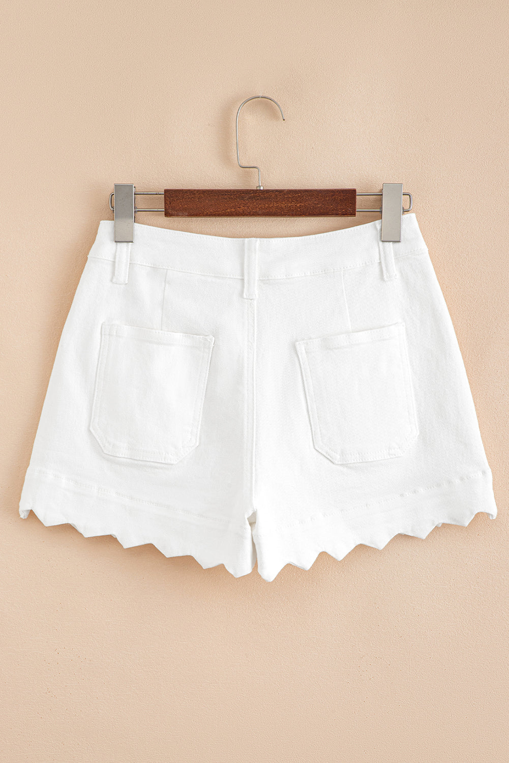 White shorts on a wooden hanger against a beige background