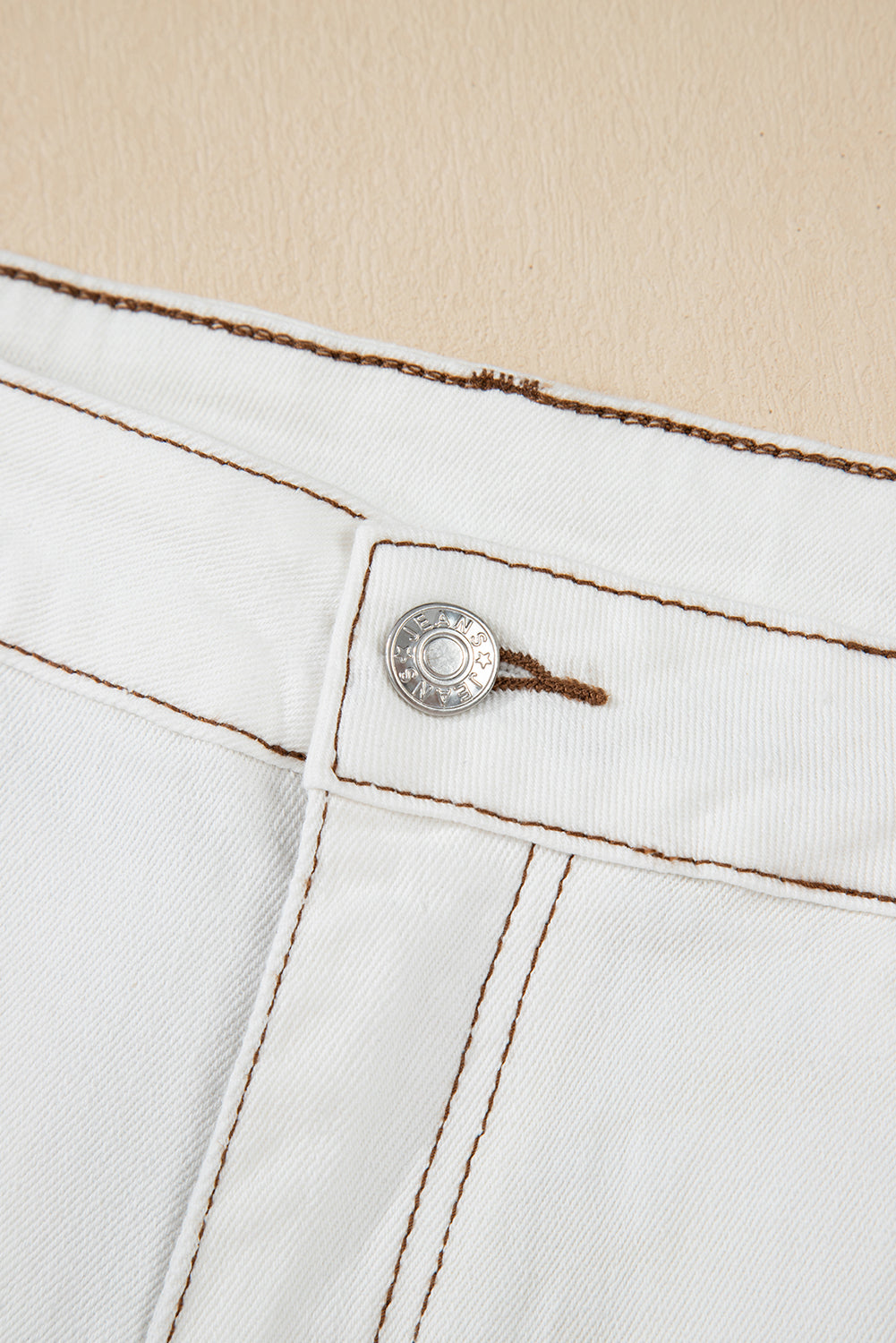 Close-up of a white denim button with brown stitching on a beige background