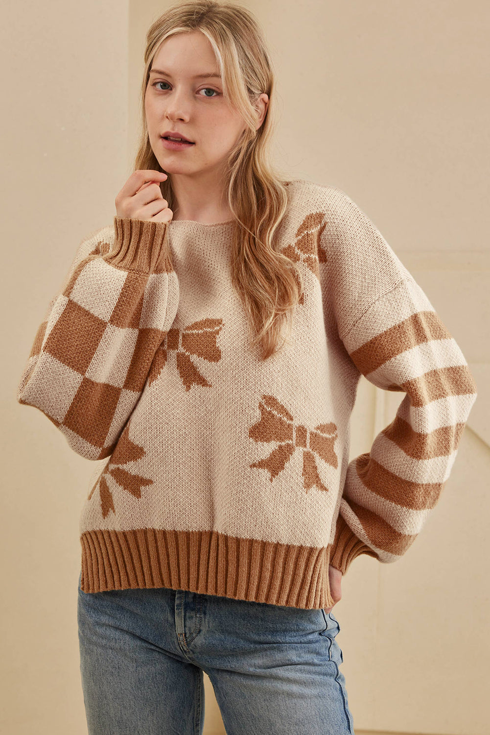 Woman wearing a beige sweater with brown bow patterns and blue jeans on a beige background