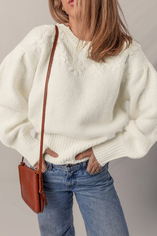 Person wearing a white sweater and blue jeans with a brown leather bag on a plain background