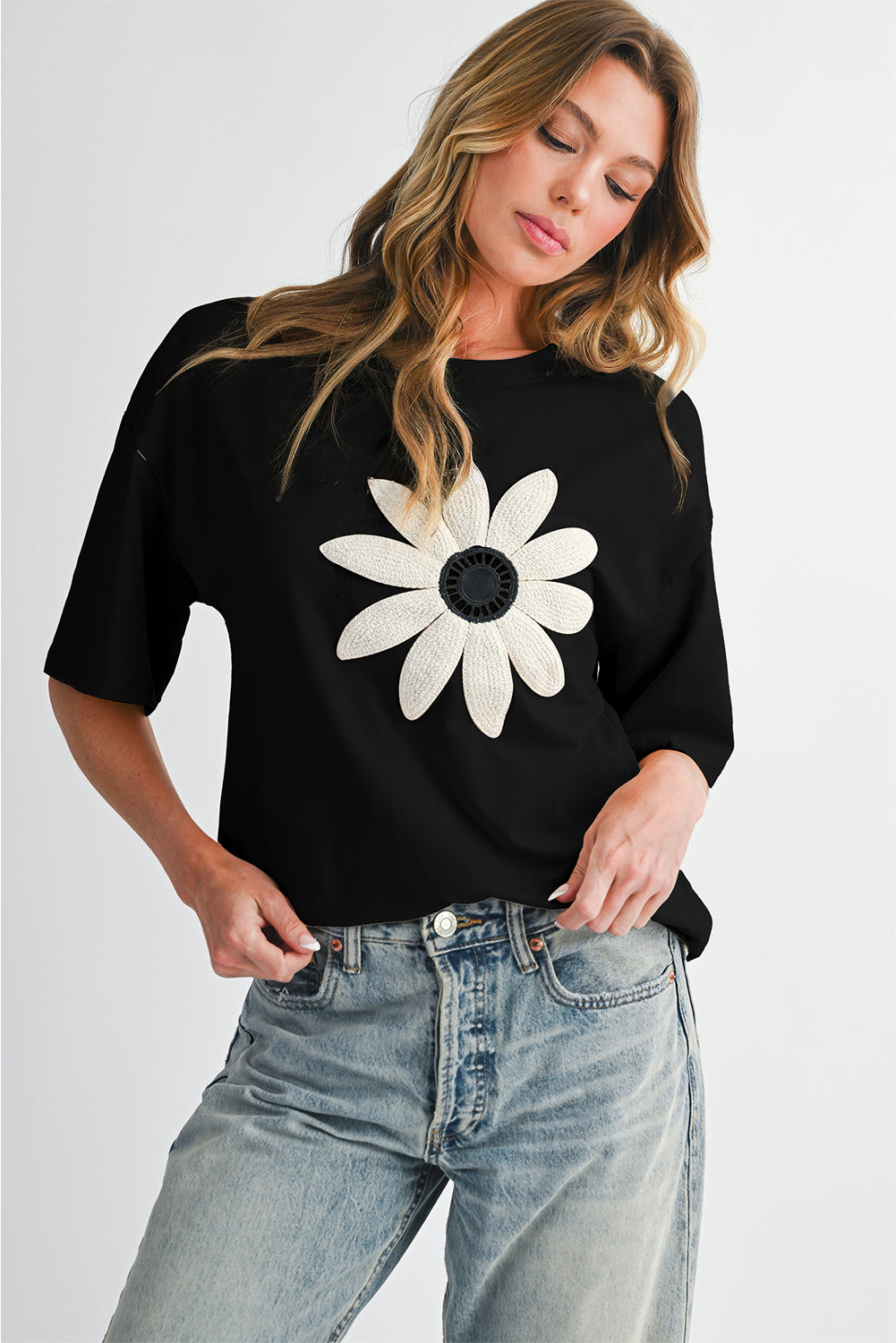 Woman wearing a black t-shirt with a white flower design on a plain background
