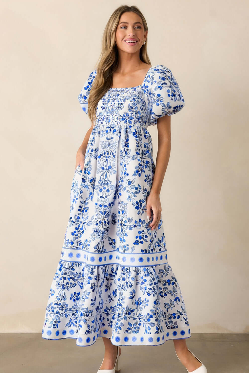 Woman wearing a blue and white floral puff sleeve maxi dress with a smocked bodice.