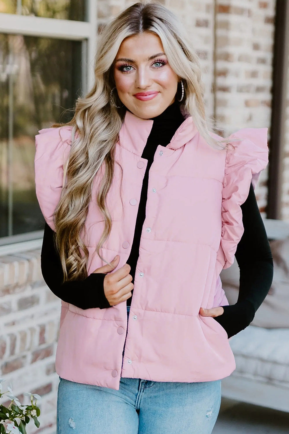 Woman wearing a pink puffer vest over a black top with a blurred background