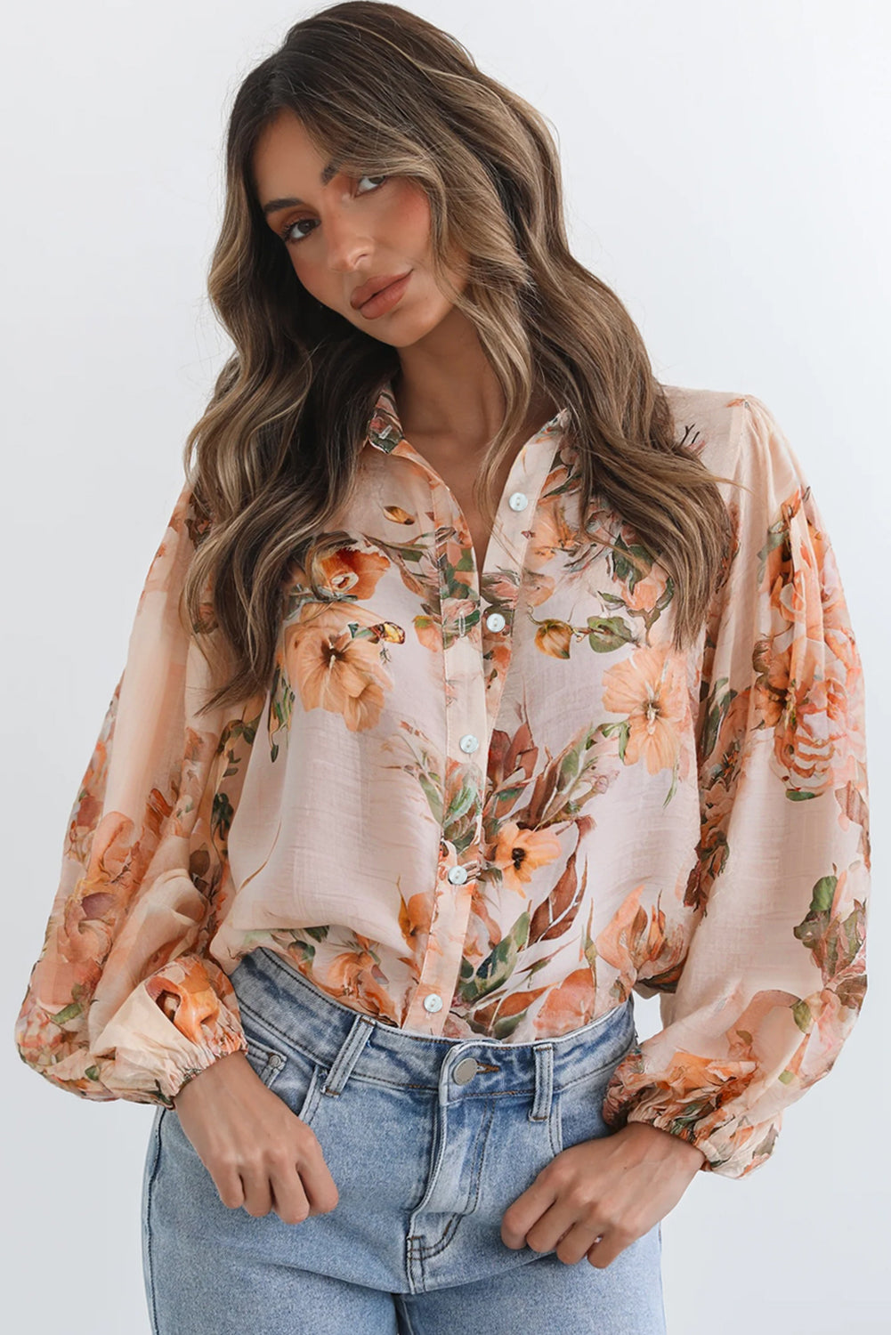Woman wearing a floral blouse with long sleeves and jeans on a white background