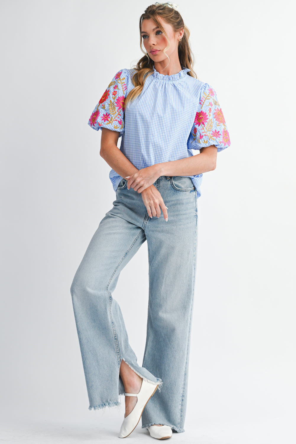 Woman wearing a light blue top with floral sleeves and high-waisted jeans on a white background
