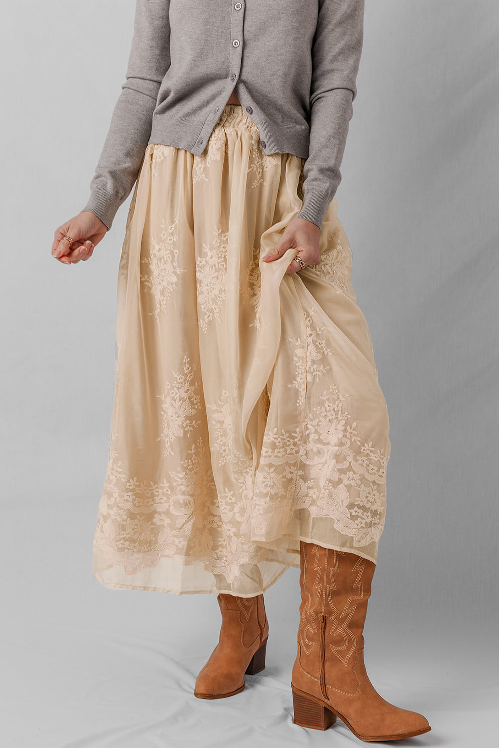 Person wearing a beige lace skirt with brown boots on a gray background