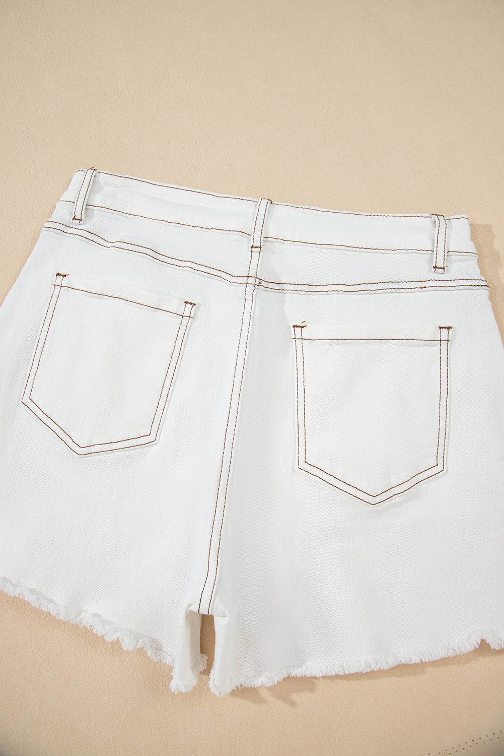 White denim shorts with frayed hem on a beige background
