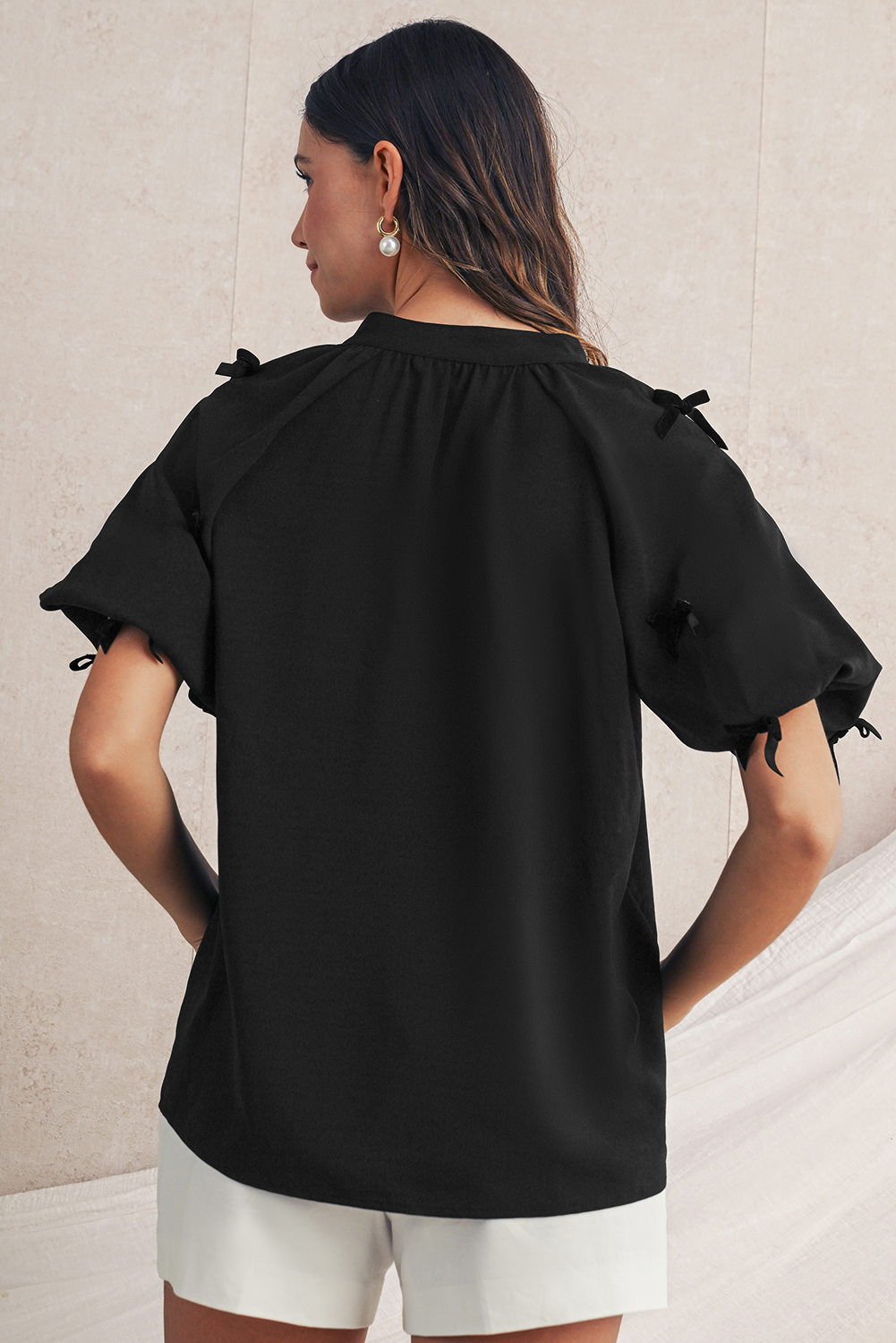 Woman wearing a black blouse with bow details on a neutral background