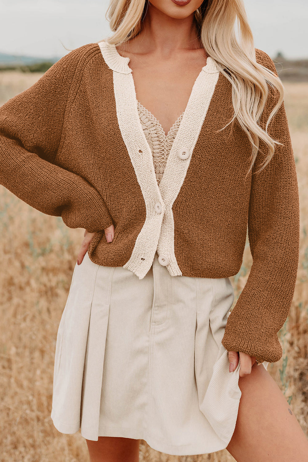 Woman wearing a brown cardigan over a beige dress in a field