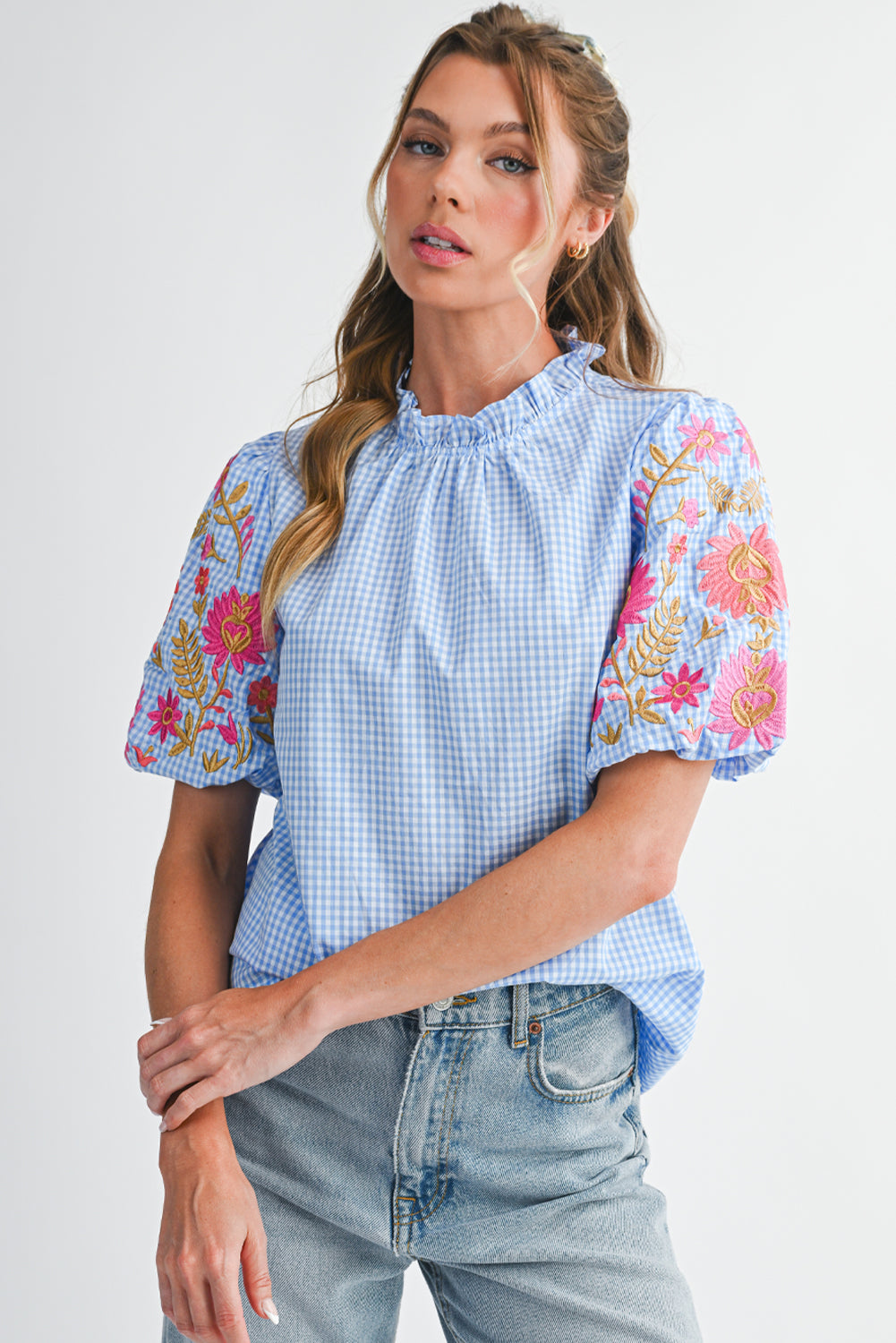 Woman wearing a blue checkered blouse with floral sleeves and denim jeans on a white background