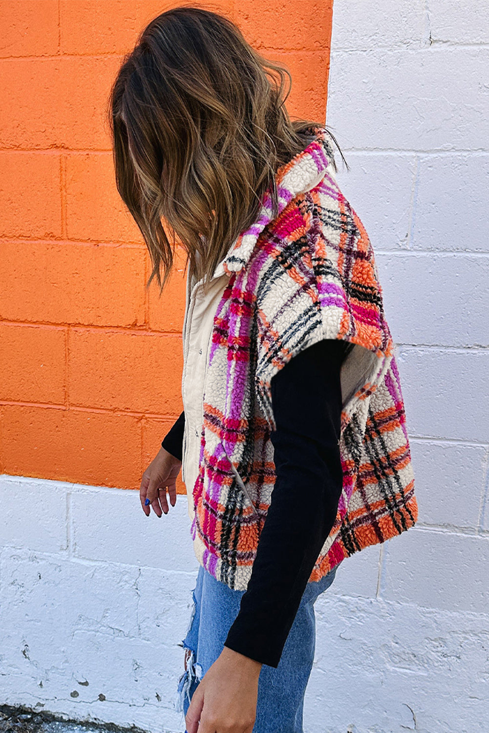 Person wearing a colorful plaid shawl against an orange and white wall.