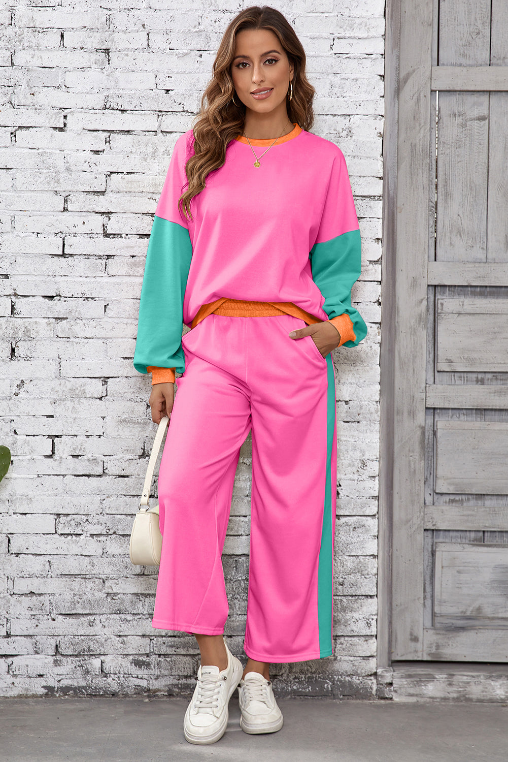 Woman wearing a pink and green outfit against a white brick wall.