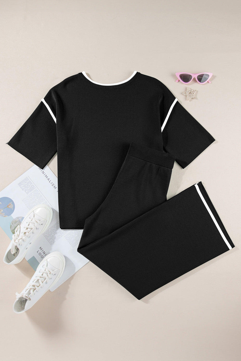 Black outfit with white accents on a beige surface with sunglasses and shoes.