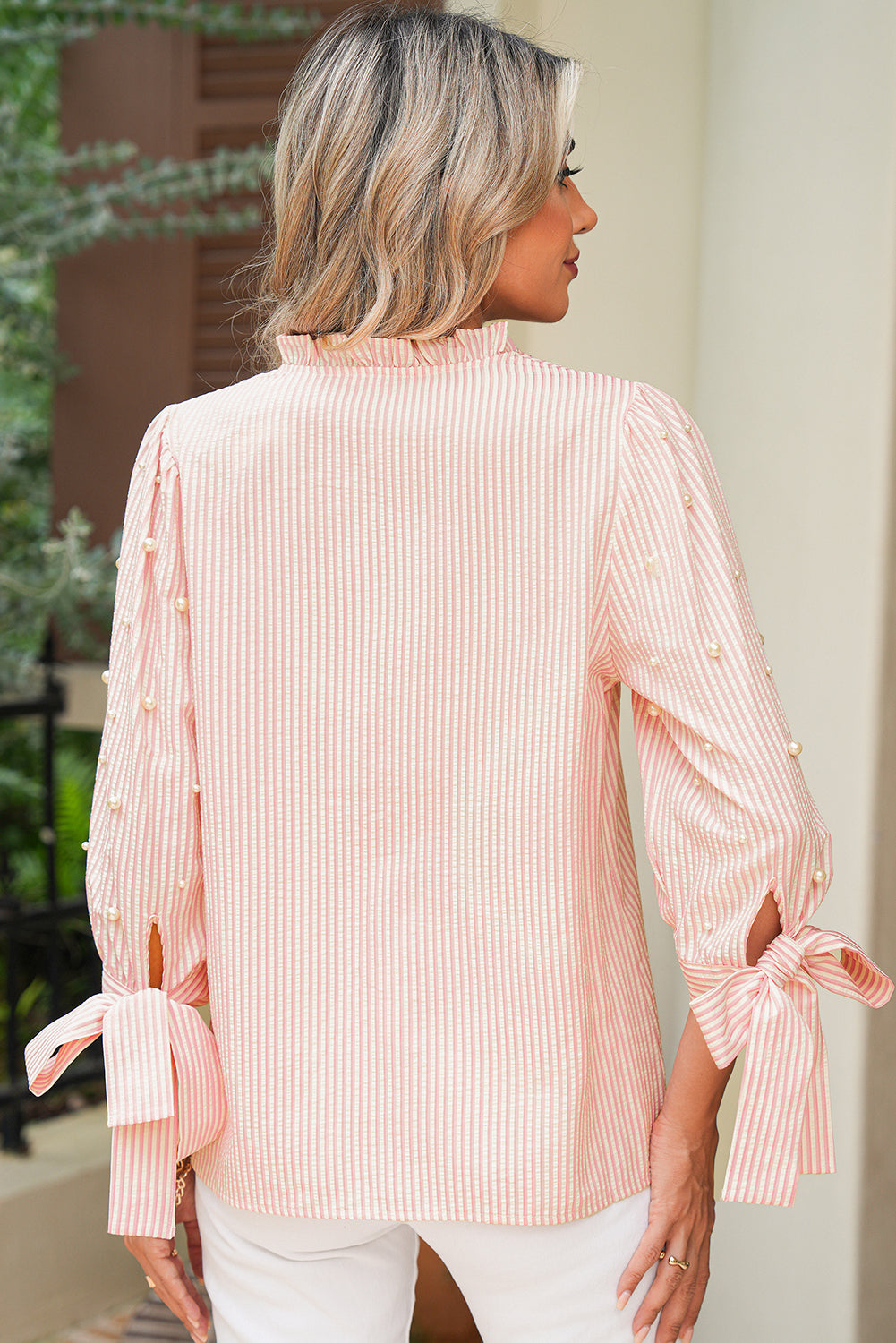 Woman wearing a pink striped blouse with tied sleeves outdoors.