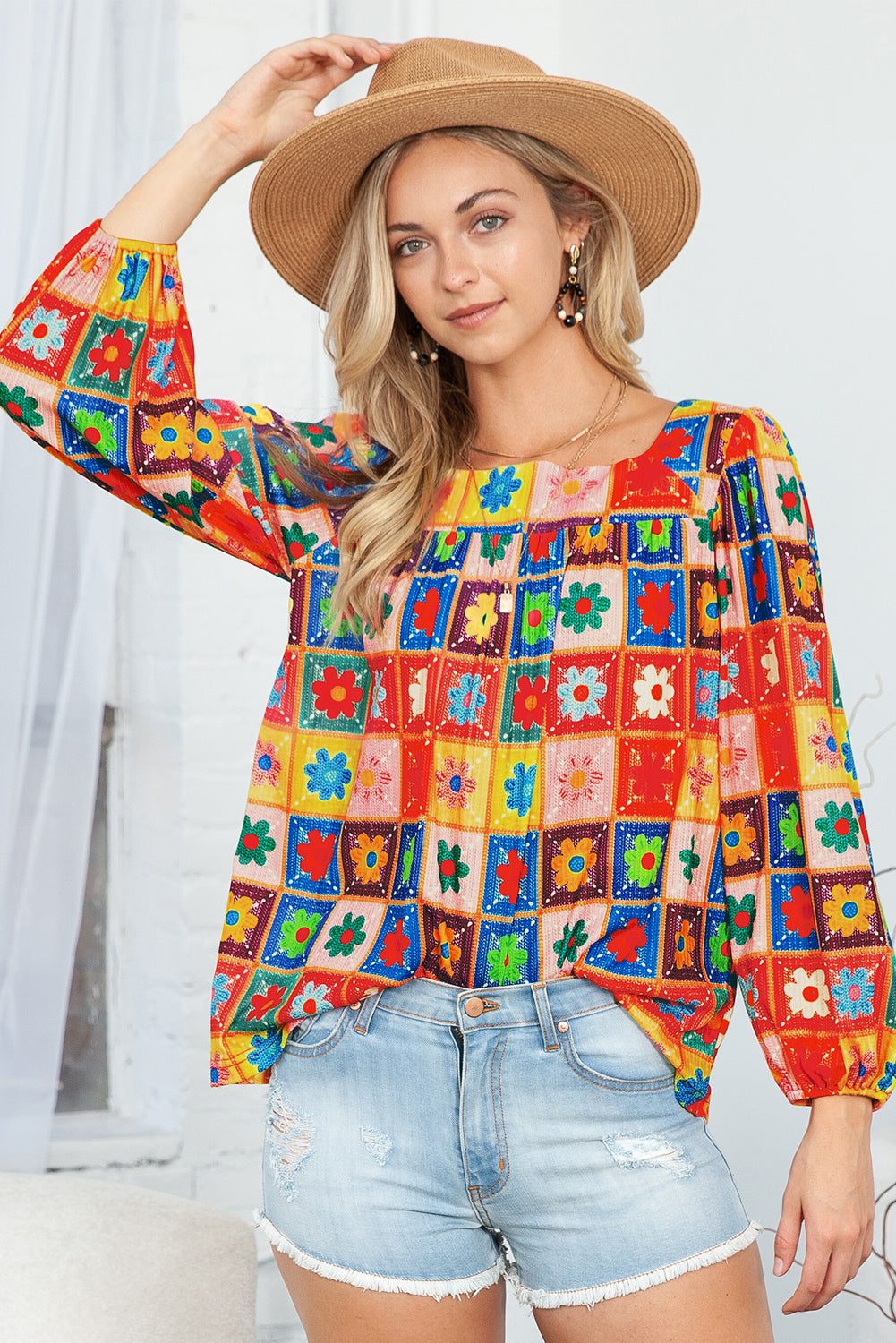 Woman wearing a colorful patterned top and denim shorts with a straw hat.
