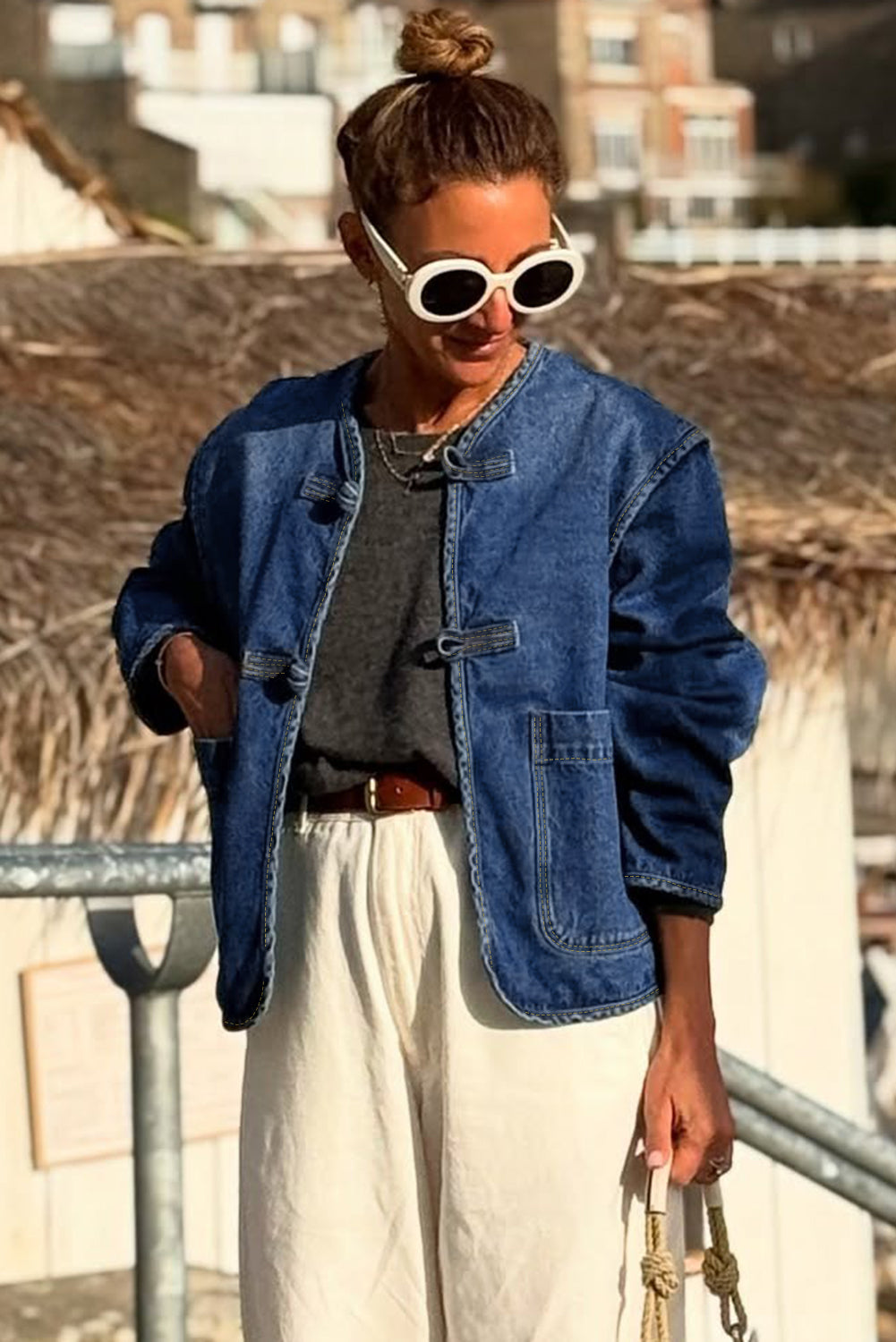 Woman wearing a blue denim jacket, gray top, and white pants outdoors.