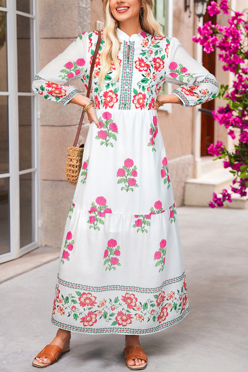 Woman wearing a floral dress with a decorative pattern, standing in front of a building with flowers.