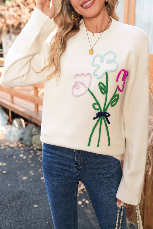 Person wearing a cream sweater with floral designs outdoors