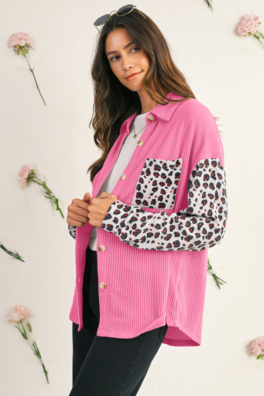 Woman wearing a pink corduroy shirt with leopard print sleeves against a light background with flowers.