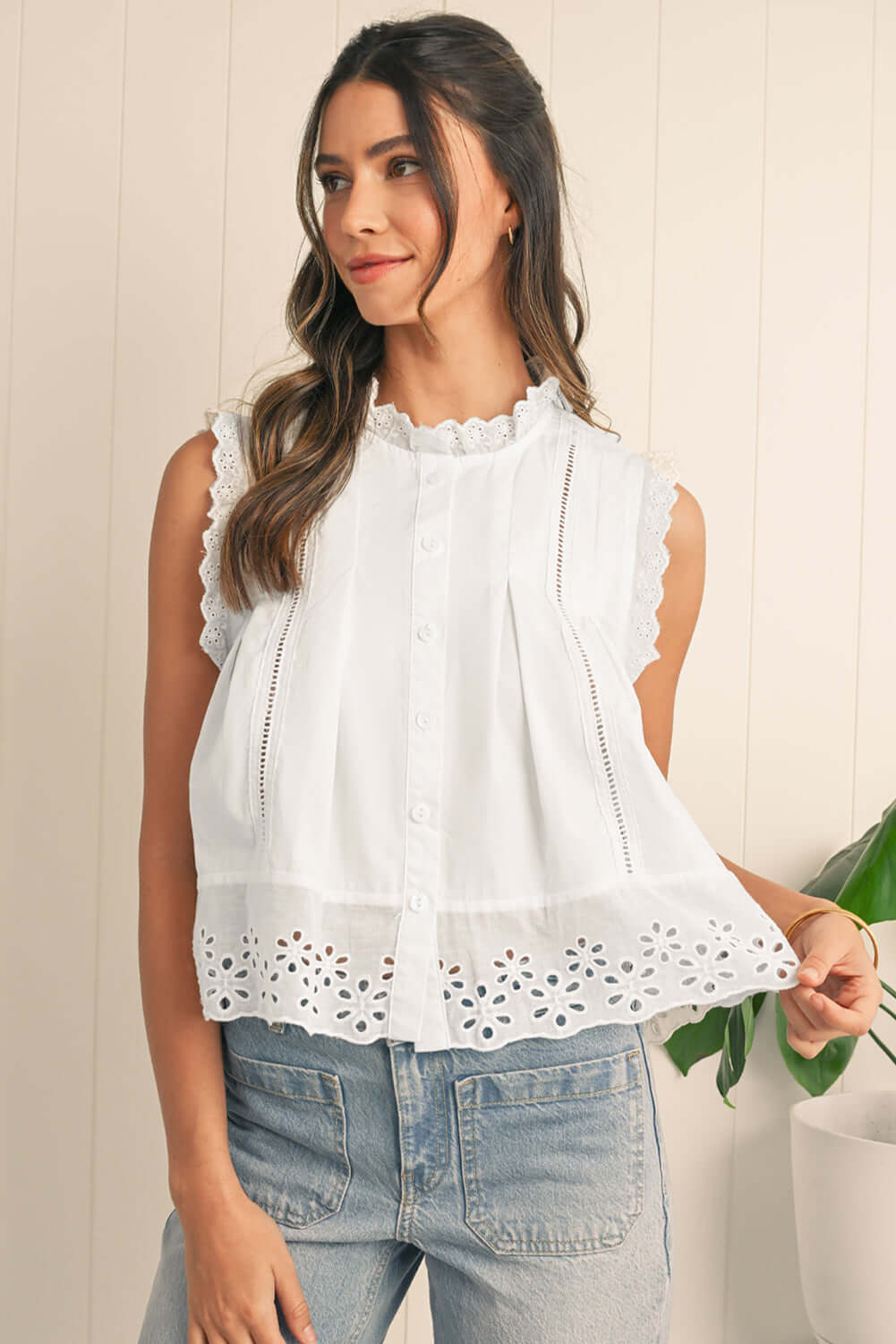 Woman wearing a sleeveless white lace-trim blouse with eyelet details, styled with denim jeans.