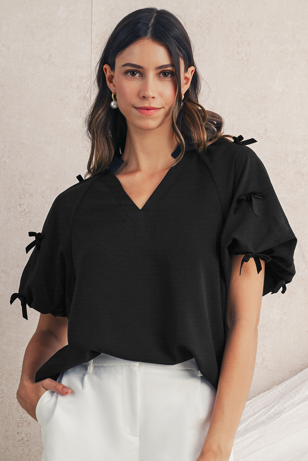 Woman wearing a black blouse with ruffled sleeves against a neutral background