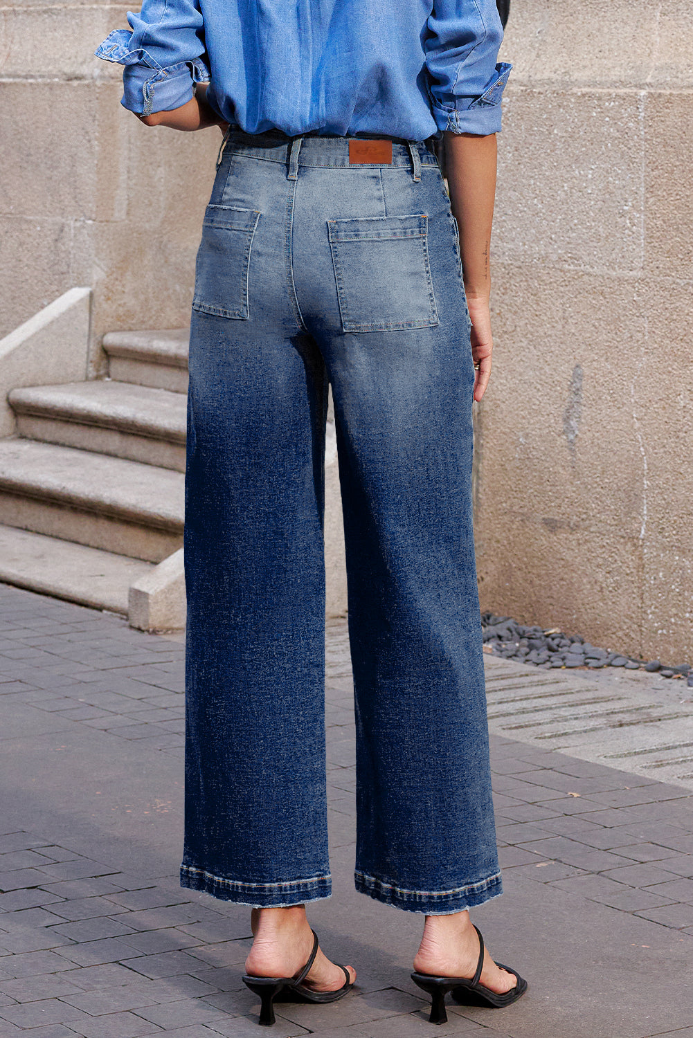 Person wearing blue jeans and a light blue shirt standing on a sidewalk.