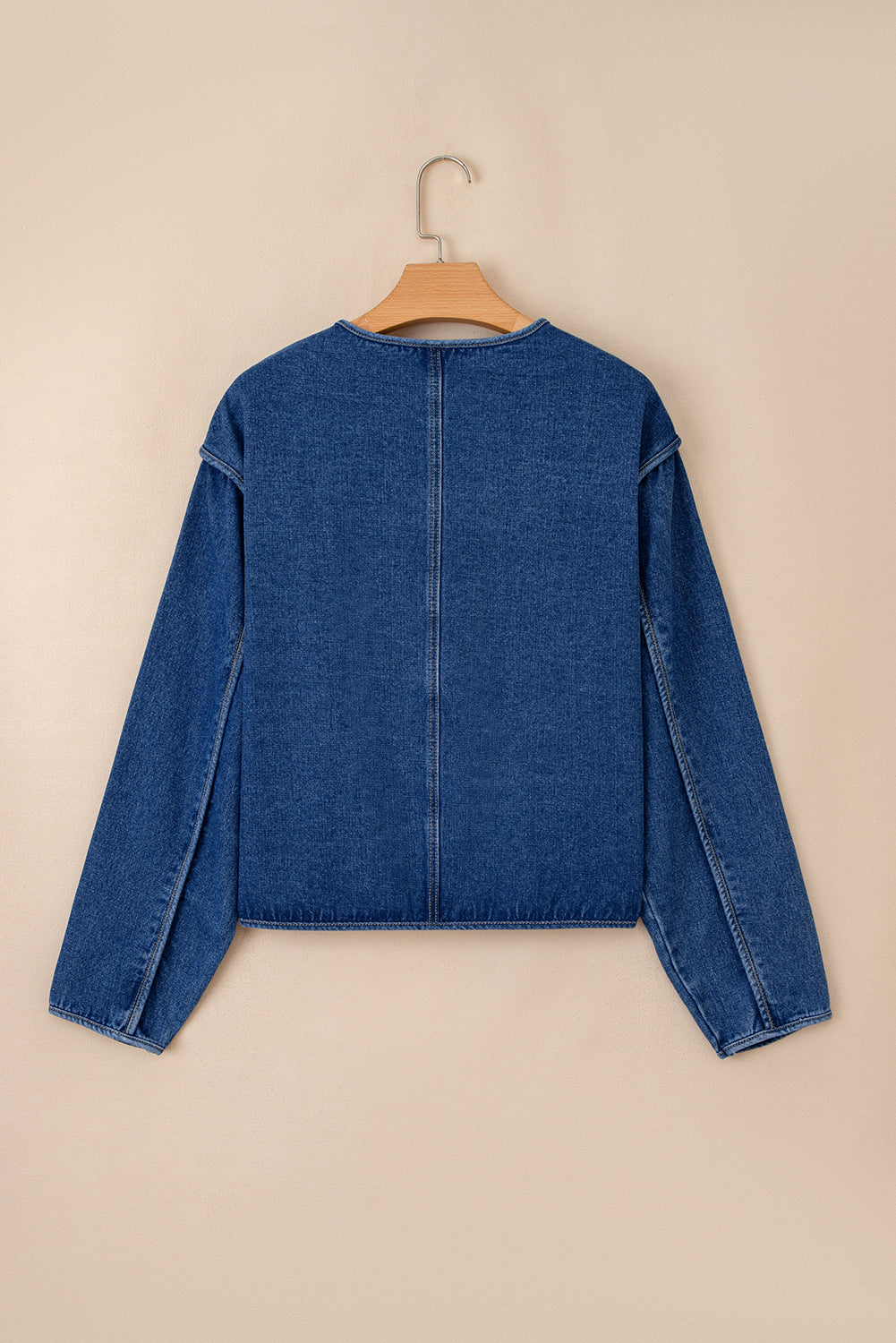 Blue denim jacket on a hanger against a beige background