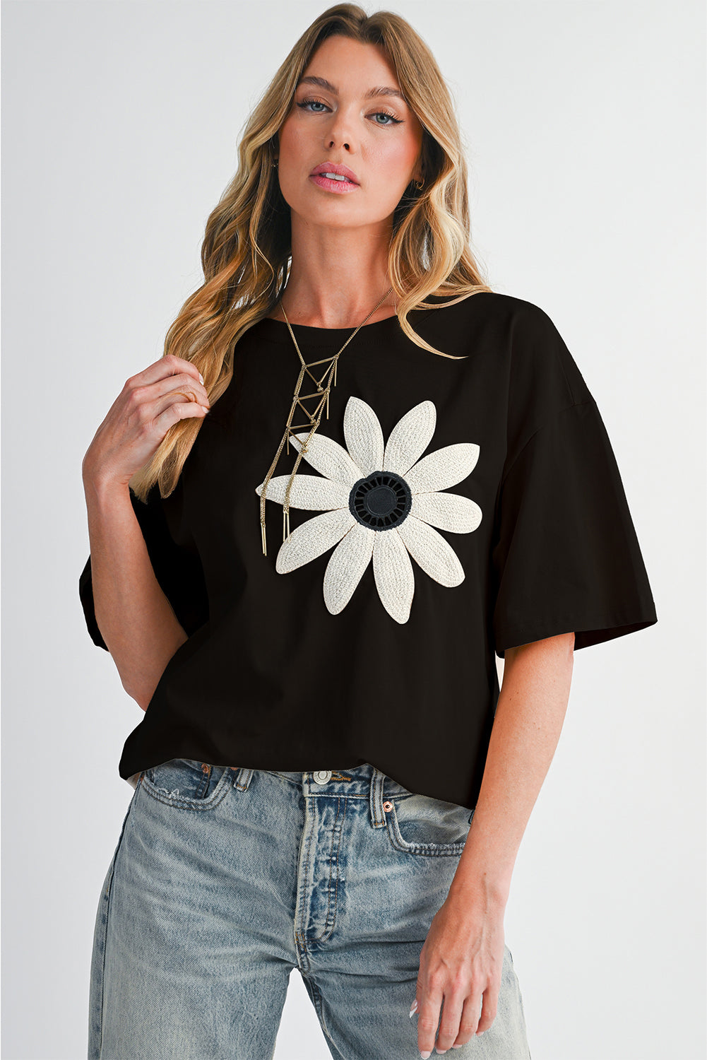 Woman wearing a black t-shirt with a white flower design on a plain background