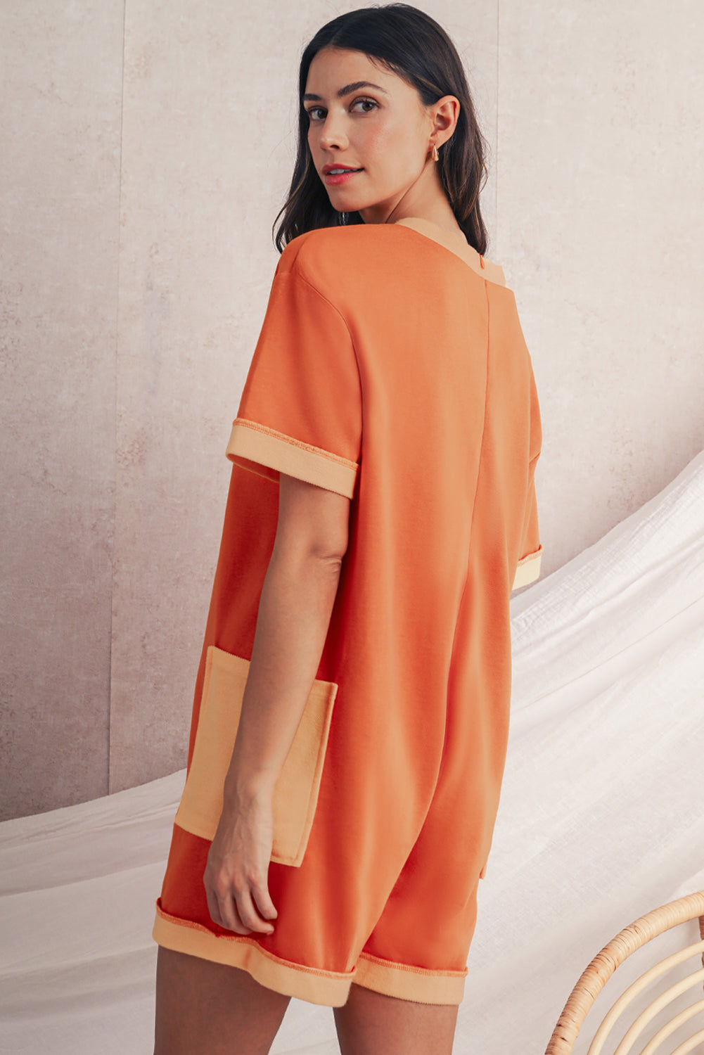 Woman wearing an orange dress with beige accents against a neutral background
