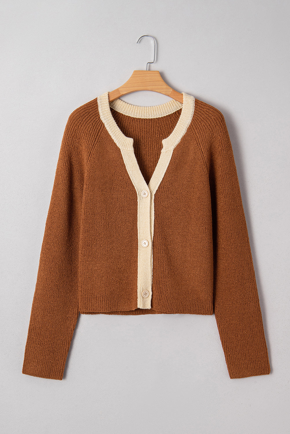 Brown sweater with cream buttons on a wooden hanger against a gray background