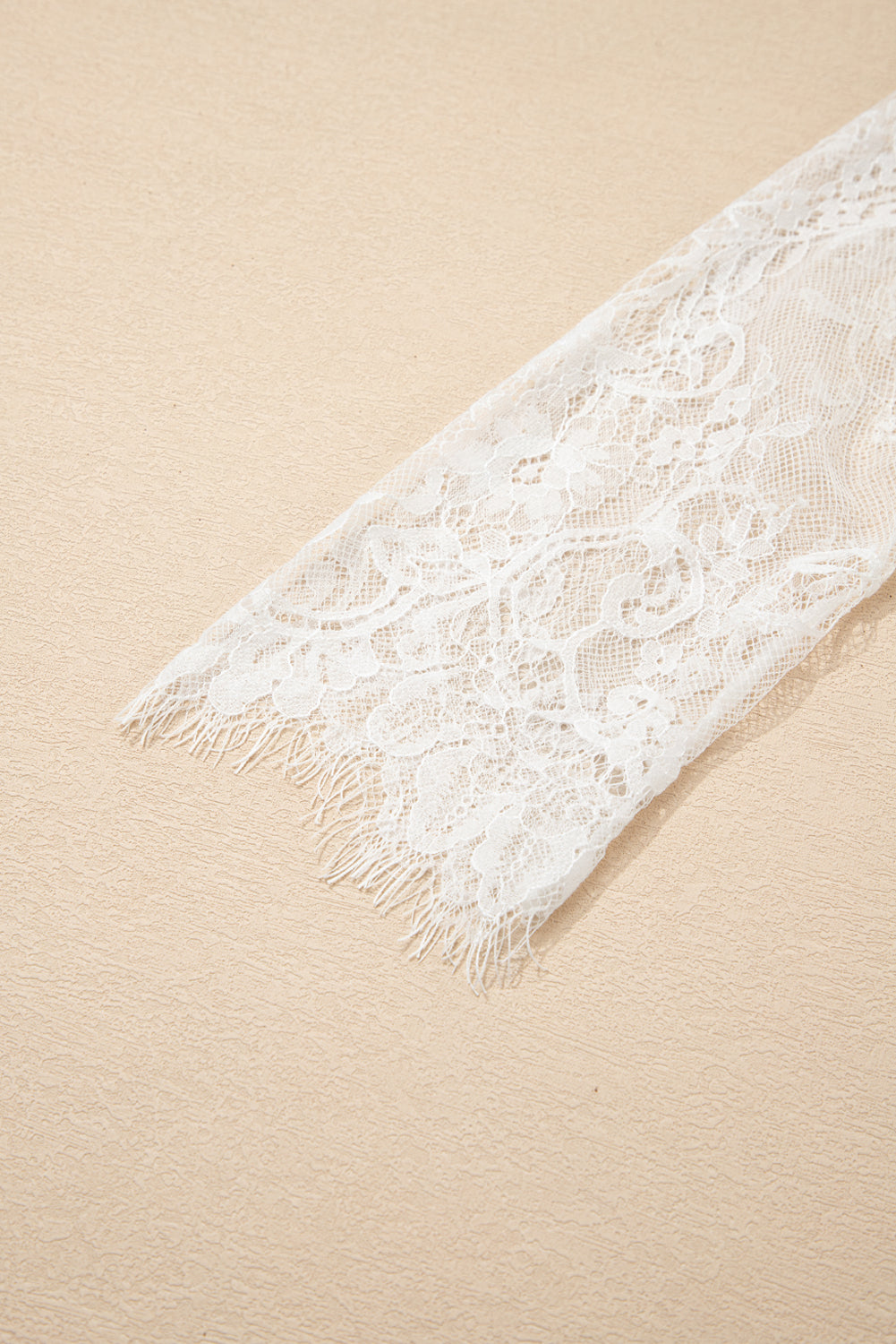 White lace fabric with fringes on a beige background