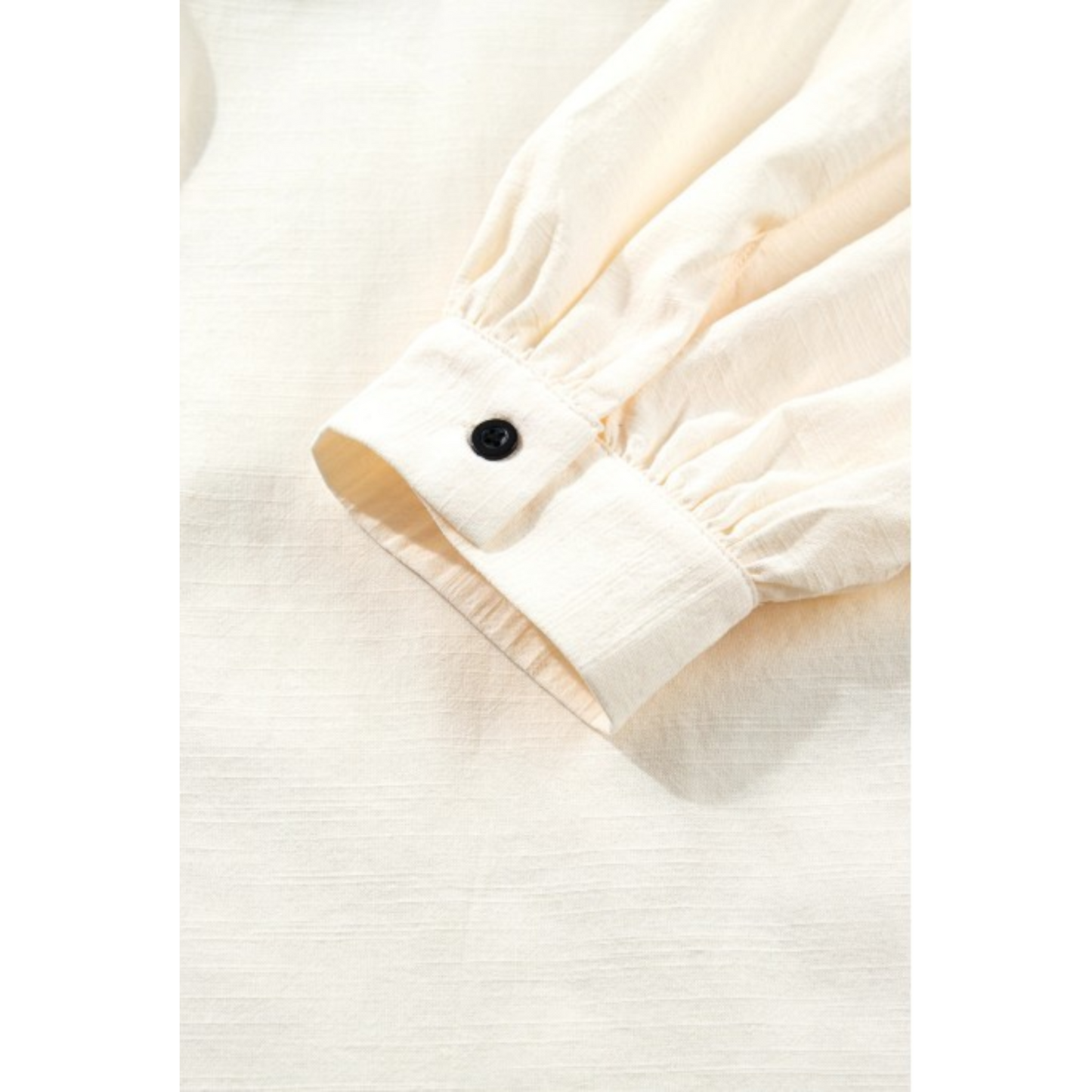 Detailed shot of the gathered bishop sleeve cuff finished with a single black contrast button and breathable cotton-blend texture.