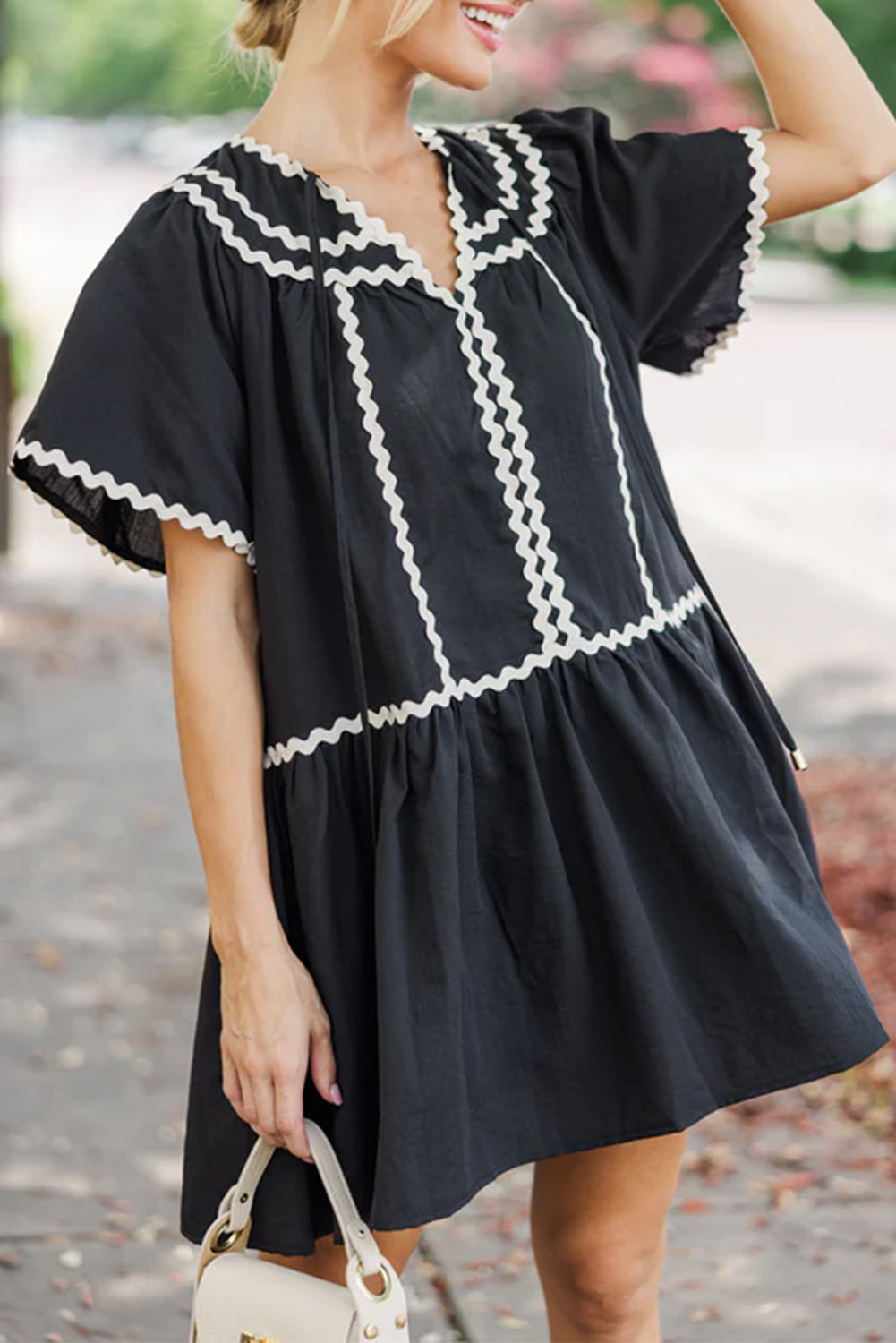 Black V-neck mini dress with ricrac detailing, knot accents, and flirty bell sleeves.