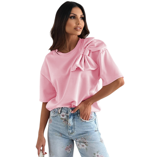 A woman wearing a vibrant pink t-shirt with a large decorative bow applique on the shoulder and relaxed drop sleeves.