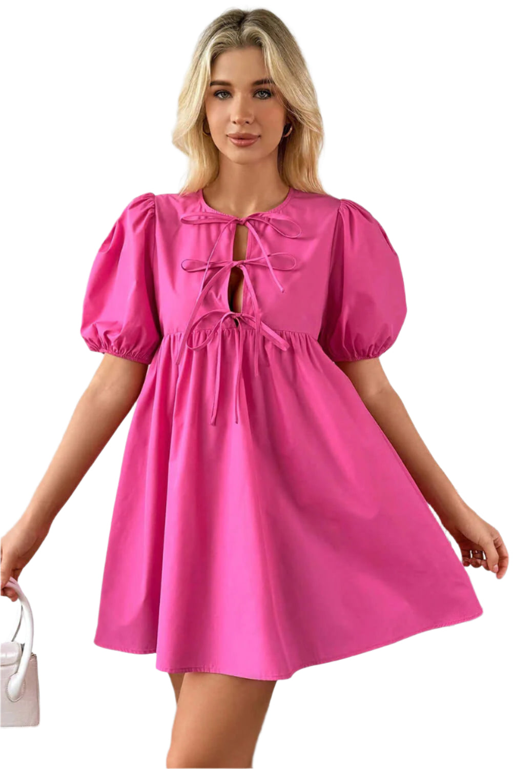 Woman in a bright pink puff sleeve mini dress with a tie front detail, styled for a bold and feminine look, holding a white handbag indoors.