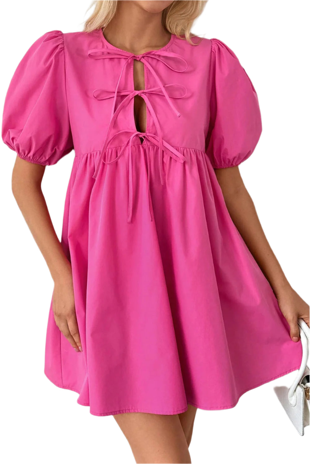 Woman wearing a bright pink puff sleeve mini dress with a tie front design, styled for a chic and playful look, paired with a white clutch.