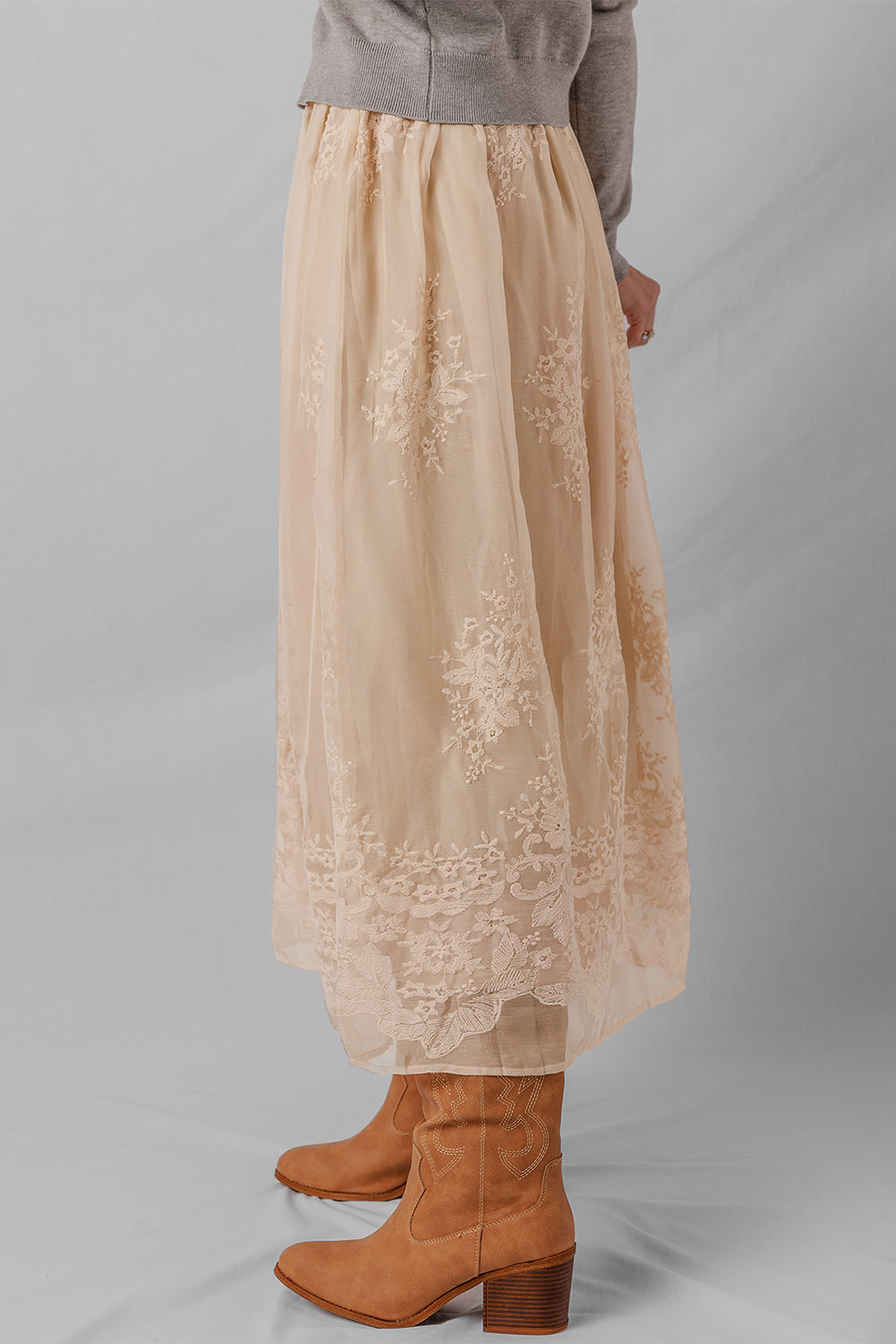 Beige lace skirt worn with brown boots on a plain background