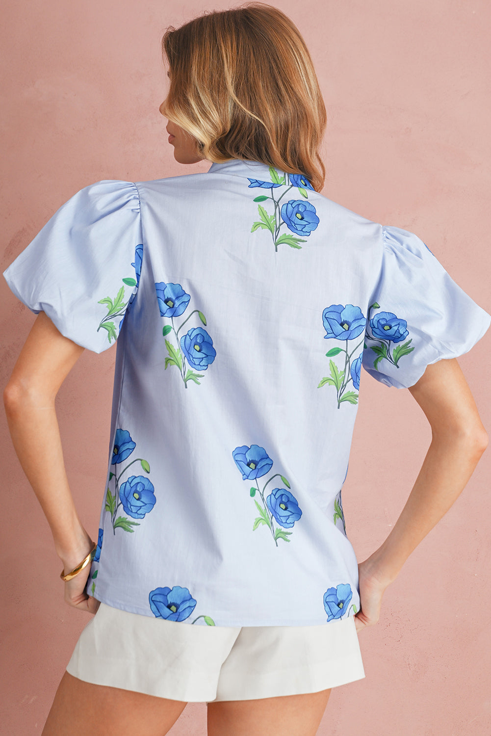 Woman wearing a light blue blouse with floral patterns on a pink background