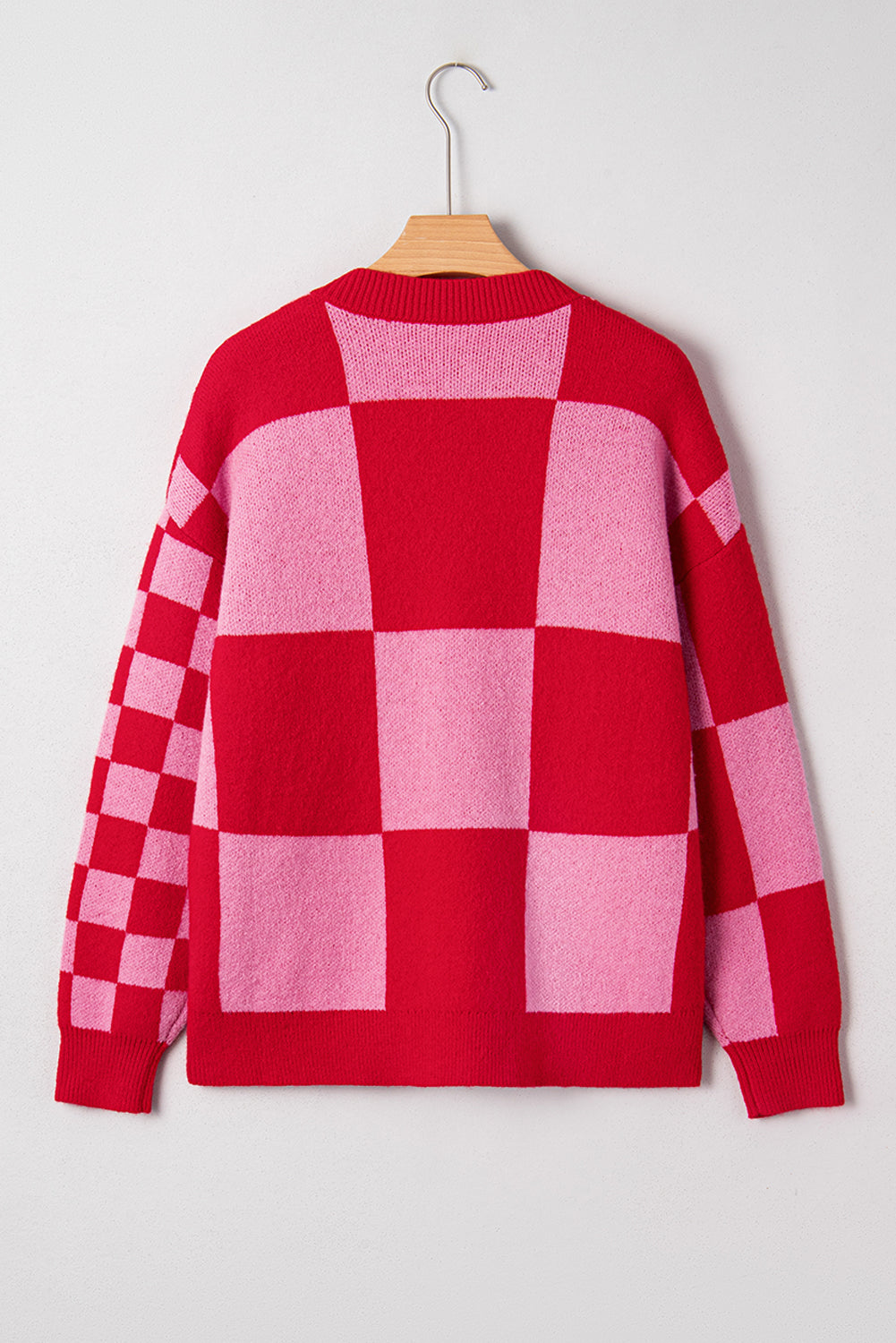 Red and pink checkered sweater on a hanger against a white background