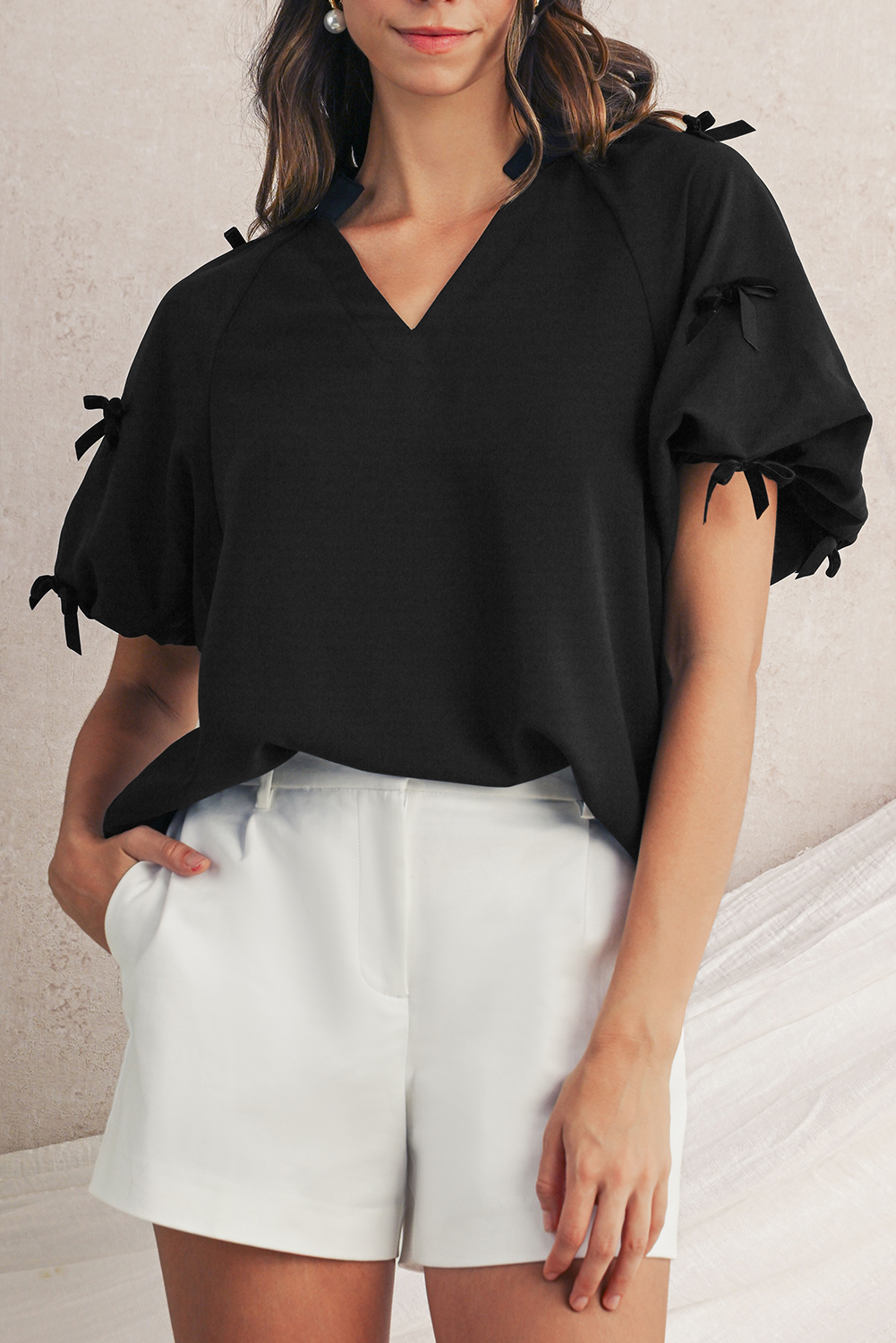 Woman wearing a black blouse with puff sleeves and white shorts against a neutral background