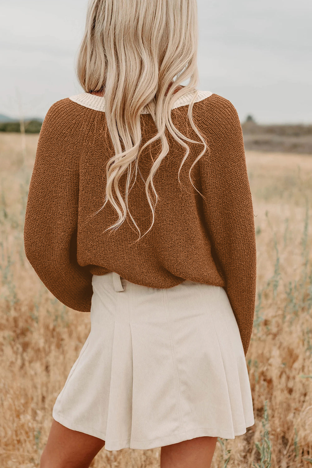 Person wearing a brown sweater and white skirt standing in a field