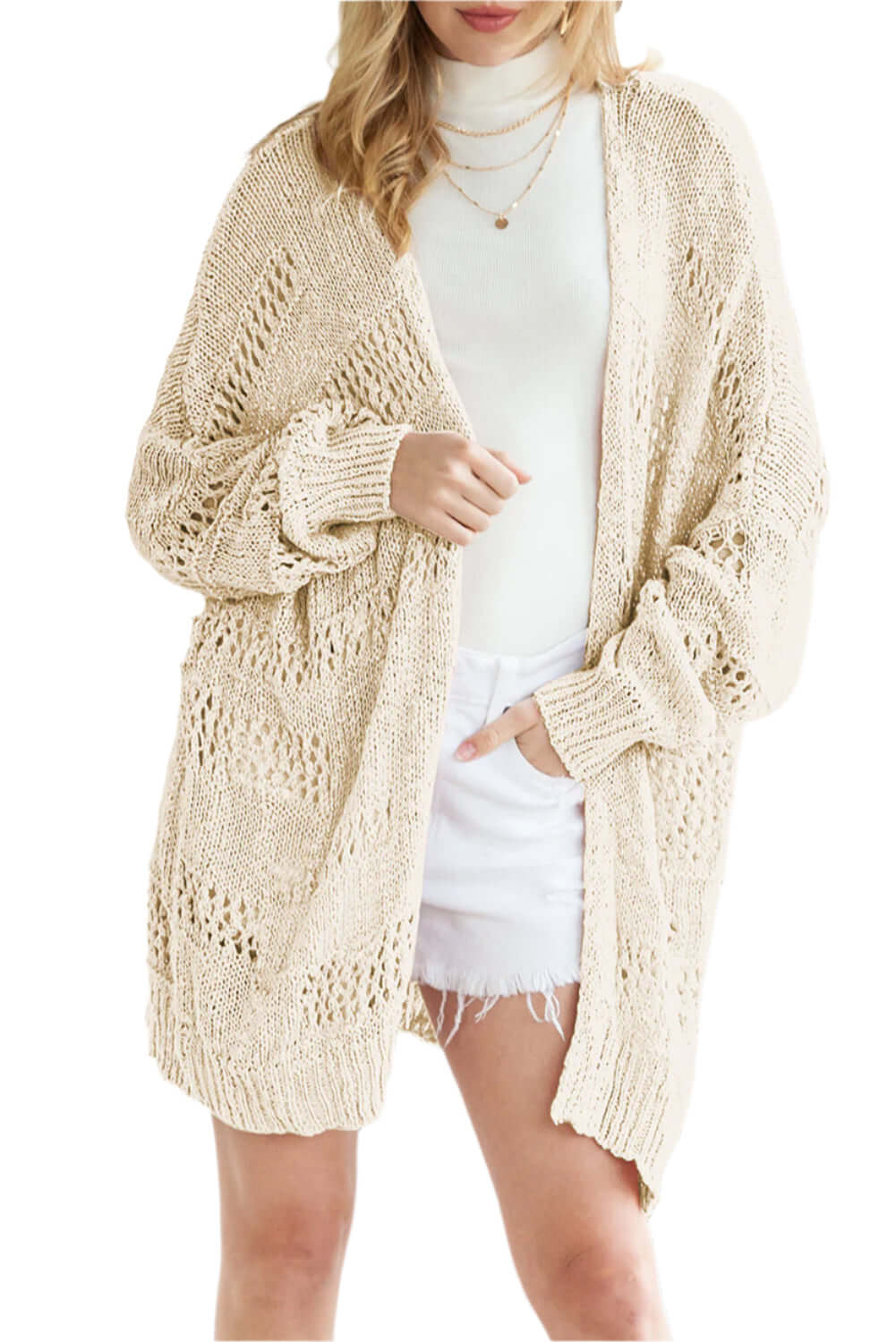 Woman wearing a beige open-knit cardigan over a white top and denim shorts.
